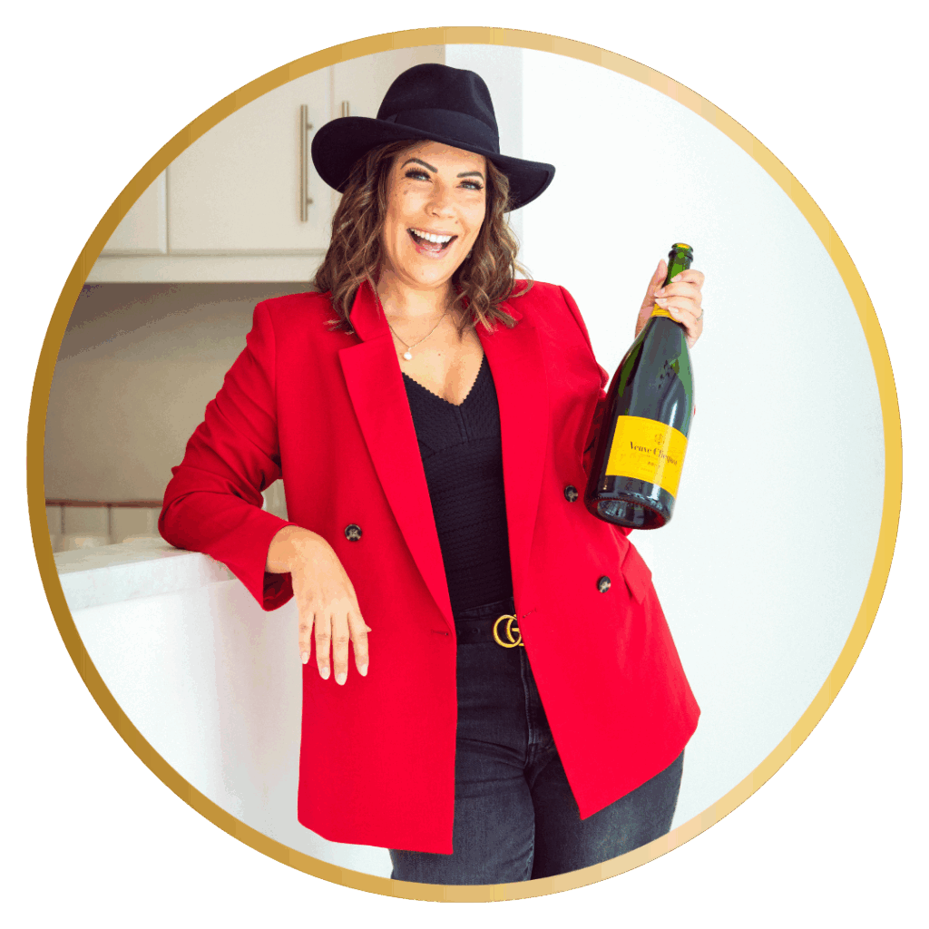 Nicole Geddes in a black hat with a red jacket holding a bottle of champagne