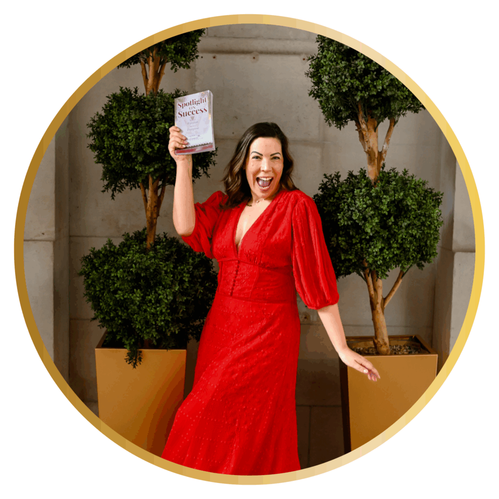 Nicole Louise Geddes, PerformerPreneur founder, holding Spotlight on Success book while celebrating in red dress at book launch