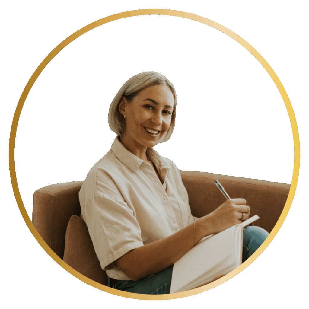 Professional headshot of Kat Cuthbert, psychotherapist, smiling warmly while seated in a tan armchair holding a notebook and pen. Kat specialises in online therapy using CBT and EMDR techniques
